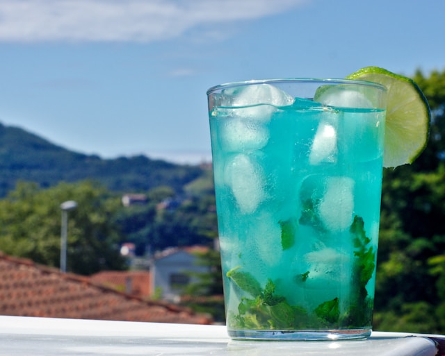 A refreshing blue mocktail with mint and lime, enjoyed outdoors with mountain views